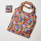 Our Coastal Floral Pocket Shopper, a lightweight foldable tote covered in bright retro daisies in orange, pink, yellow and blue on a navy background, shown open and laid flat next to its matching pouch that it folds into with a snap closure.