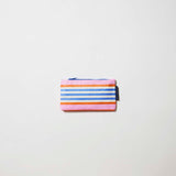 Our Capri Stripe Tiny Zip Pouch, a small flat pouch in horizontal stripes of pink, orange, blue and ecru, with a blue zip.