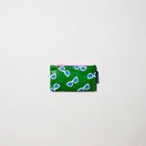 Our Sunglasses Tiny Zip Pouch, a small flat pouch in green with a scattered print of ecru framed sunglasses with blue lenses, and a pink zip.