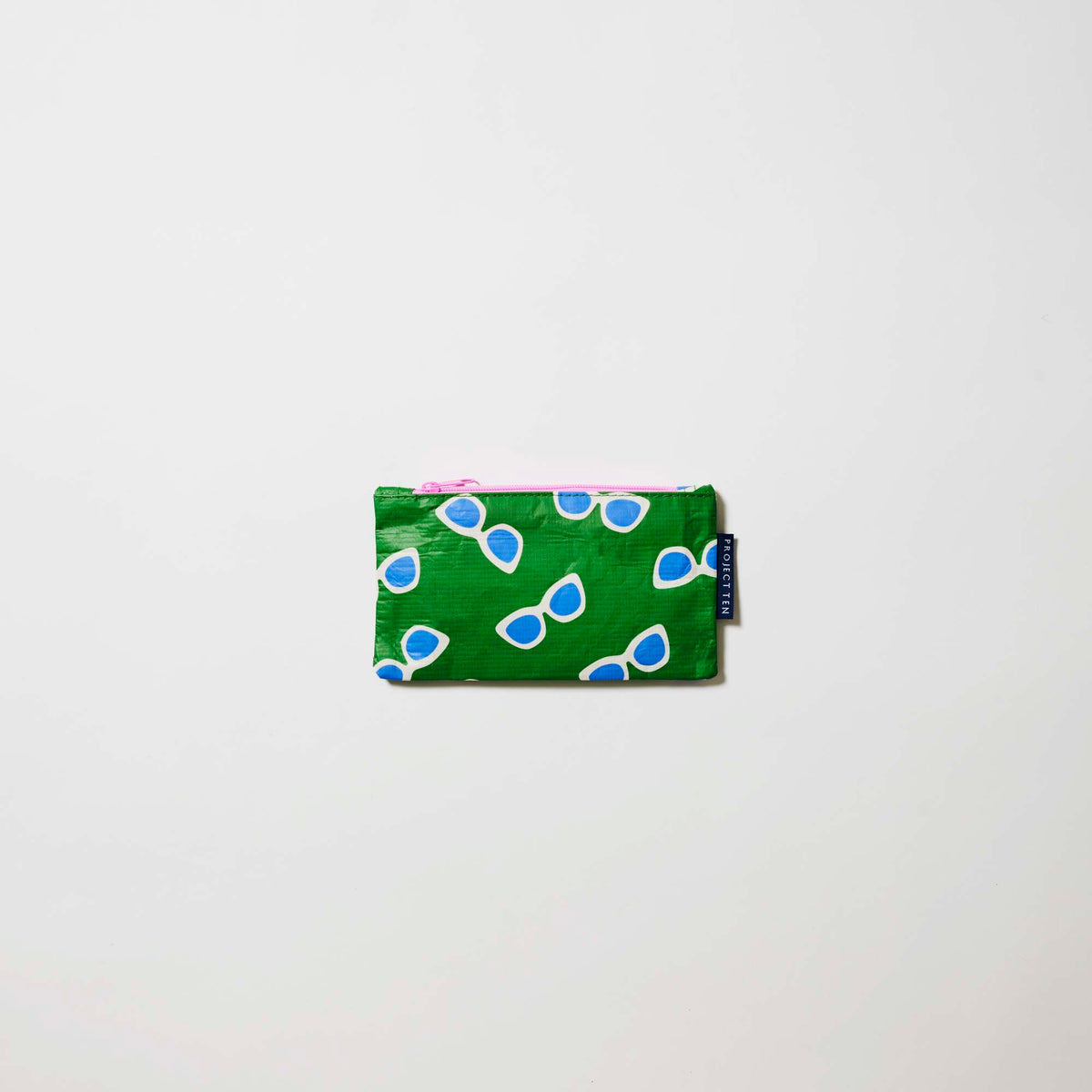 Our Sunglasses Tiny Zip Pouch, a small flat pouch in green with a scattered print of ecru framed sunglasses with blue lenses, and a pink zip.