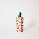 Our Holiday Cheers Wine Bag, a tall narrow bottle bag in an ecru base with a repeating geometric Christmas tree print in red, green, pink and orange, with a single green and pink striped carry handle.