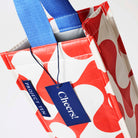 Our Red Ripple Wine Bag, a tall narrow bottle bag in a red and ecru wave print with a single blue carry handle.