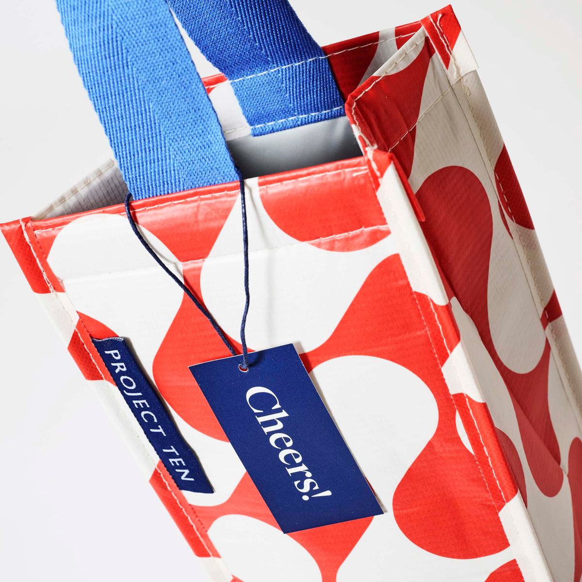 Our Red Ripple Wine Bag, a tall narrow bottle bag in a red and ecru wave print with a single blue carry handle.