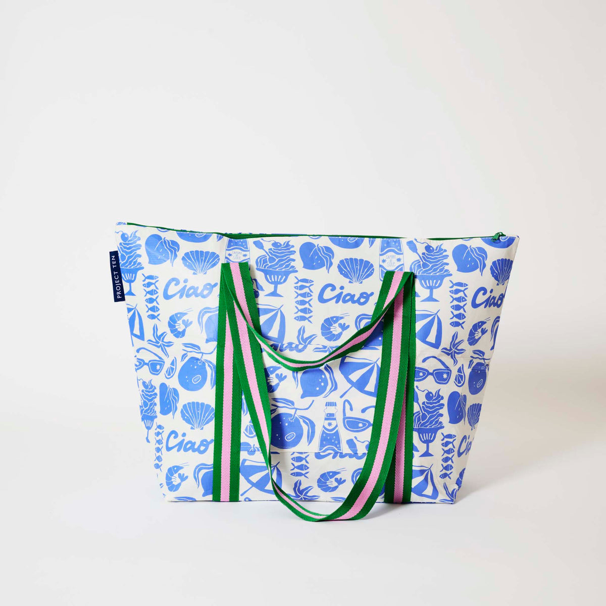 Our Feast Zip Medium Tote in a blue and ecru print of shells, gelato, soda bottles, sunglasses, beach umbrellas and the word "Ciao", with a full zip closure across the top and long green and pink striped shoulder straps.